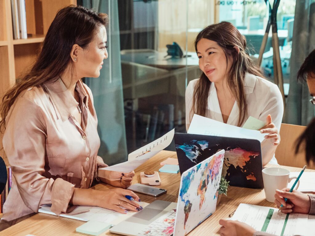 Group of colleagues discussing strategy in a modern office setting with laptops and documents.